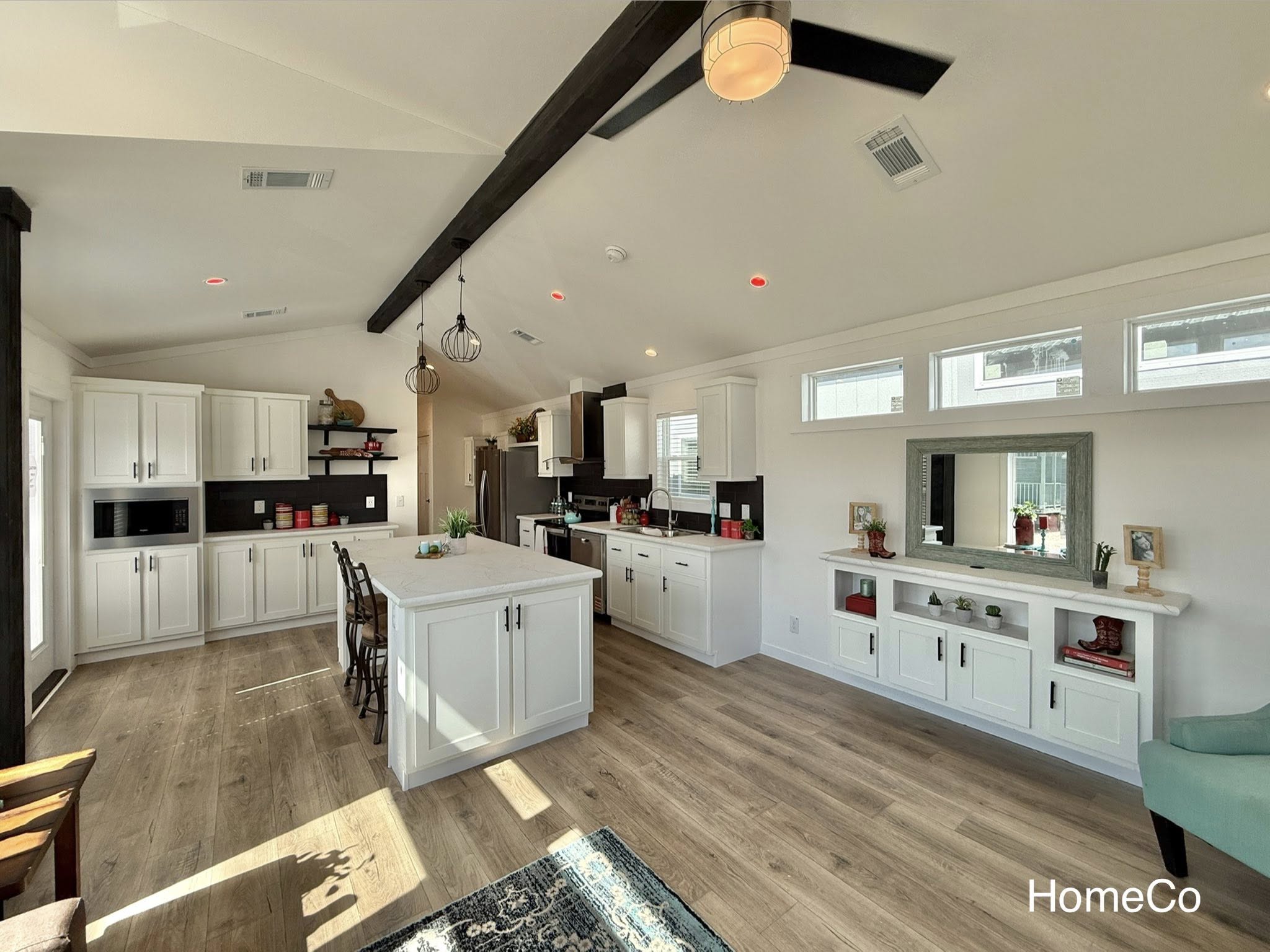Modern kitchen with white cabinets, central island, and wooden floor. Natural light from clerestory windows creates a bright, inviting space.