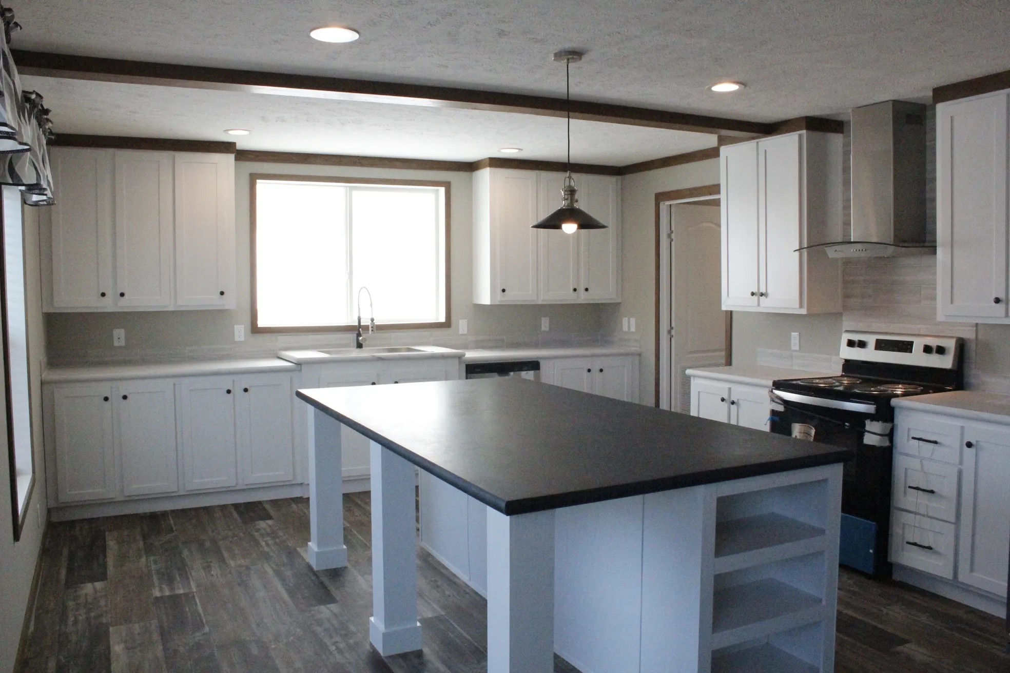 Spacious kitchen with white cabinets, large central island with dark countertop, stainless steel appliances, and a hanging light fixture.