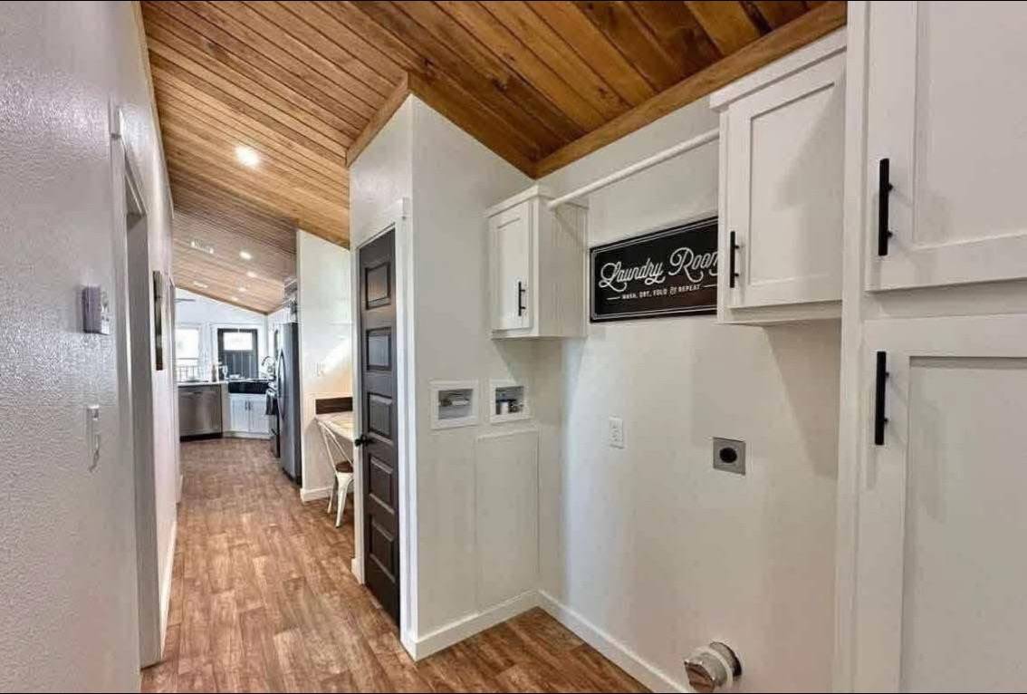 Narrow hallway with wood ceiling and floor, white cabinetry, and a "Laundry Room" sign. Kitchen visible at the end, creating a cozy atmosphere.
