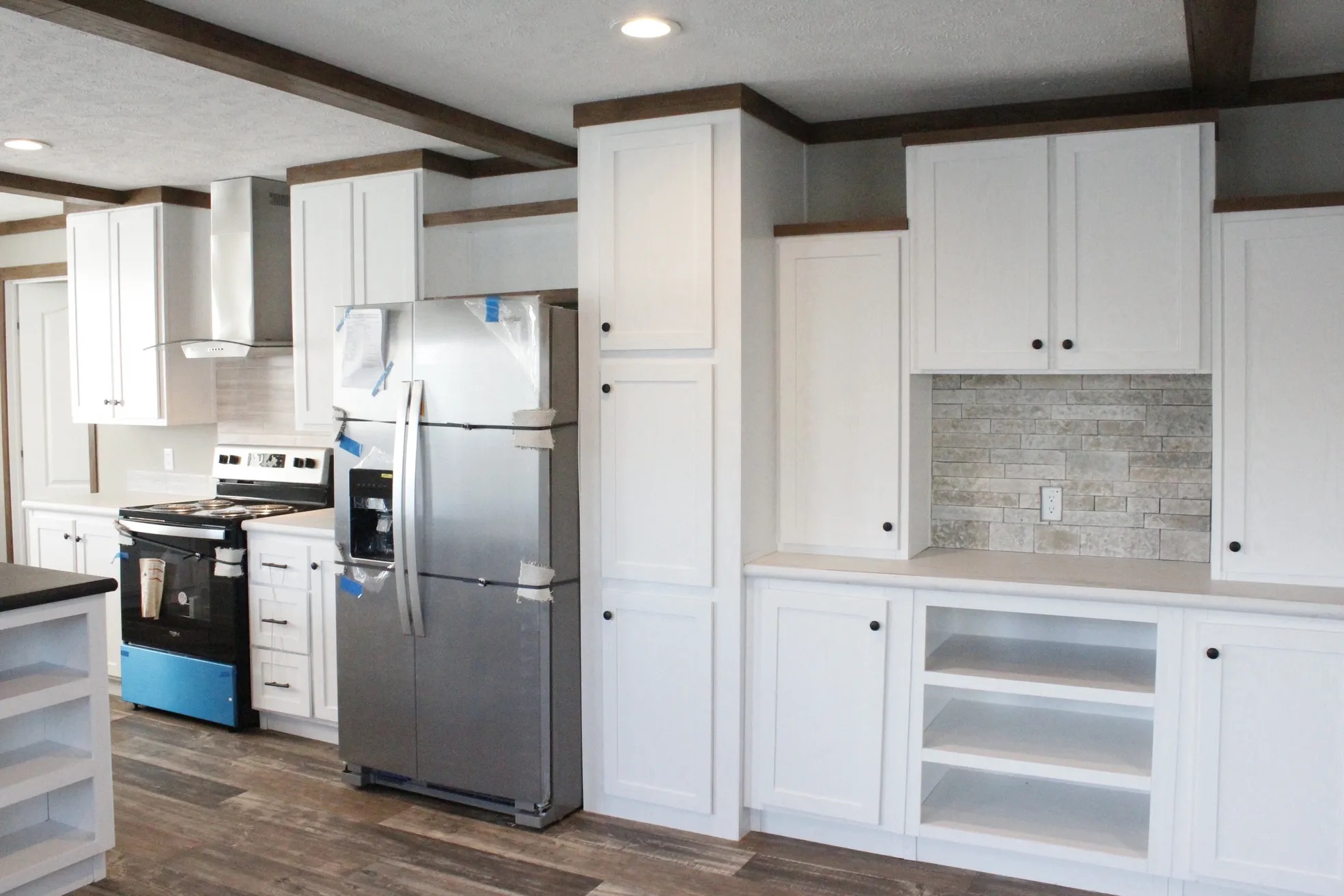 Modern kitchen with white cabinets, stainless steel fridge, and a stove. Brick backsplash and wood floors add a warm, inviting touch.