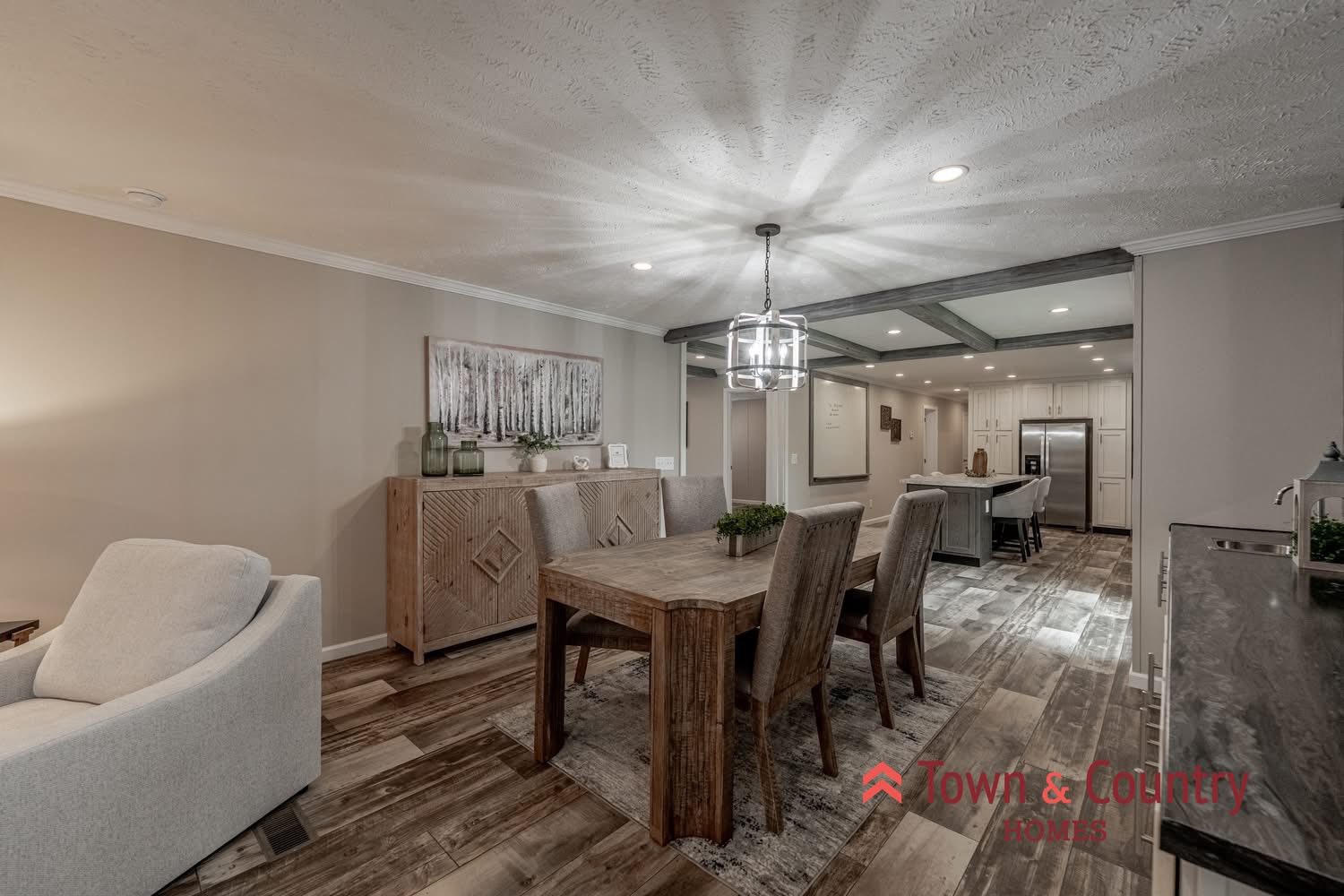 Spacious dining area with light wood flooring, a rectangular wooden table, and six upholstered chairs. Soft beige walls, modern chandelier, and nearby kitchen. Cozy, elegant ambiance.