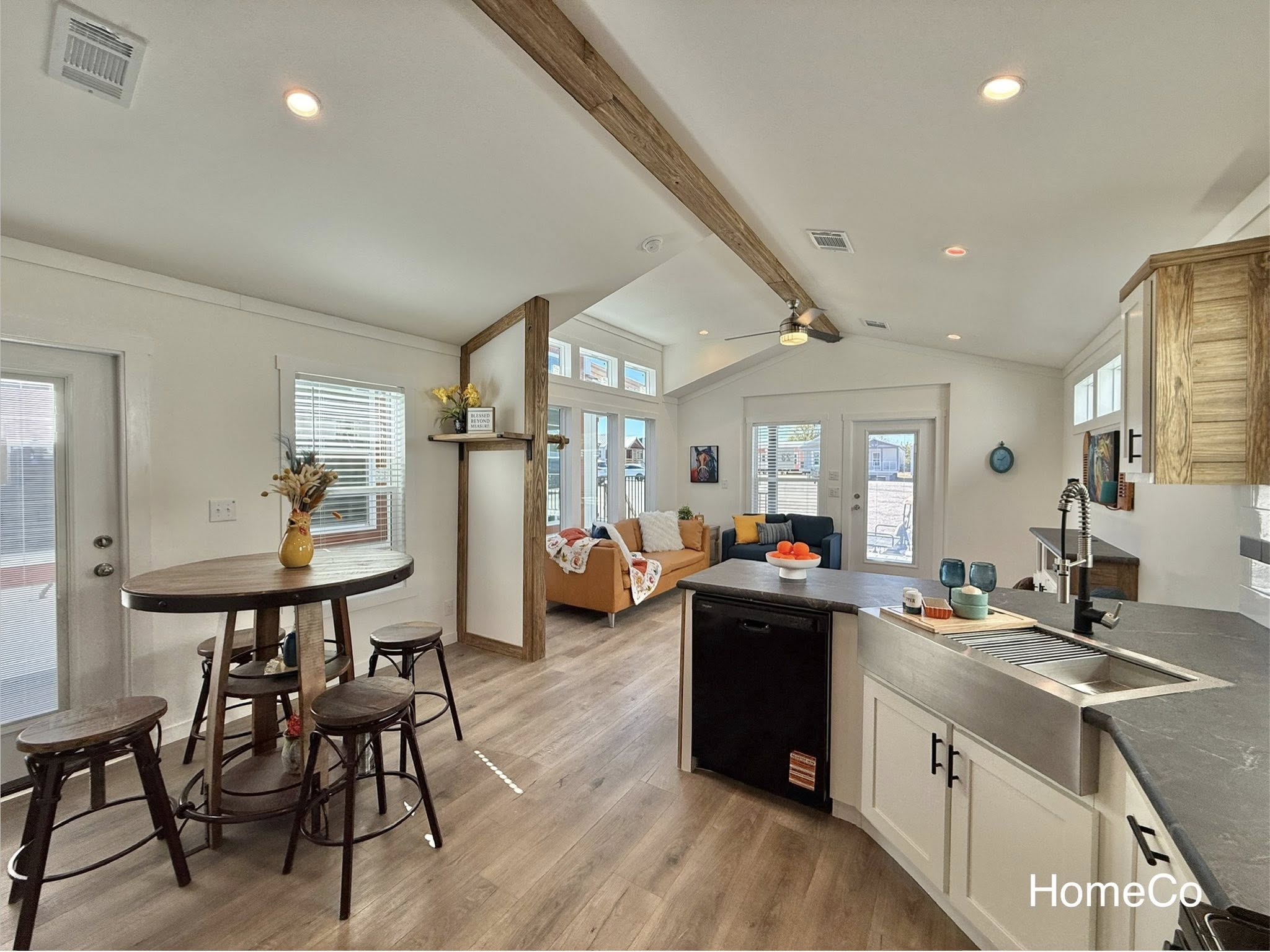 Luxury modular and tiny home showcase featuring navy blue and white farmhouse exteriors, modern white kitchens with quartz waterfall islands, hidden arched pantries, and rustic-industrial interiors with corrugated metal accents, vaulted ceilings, and loft living spaces.