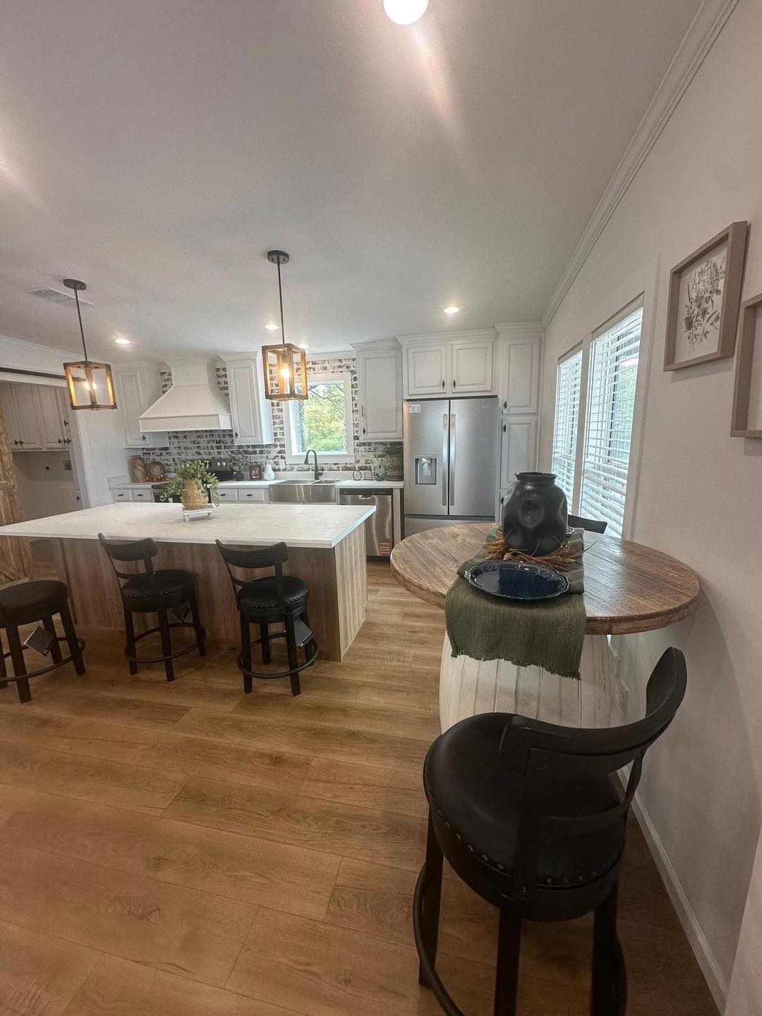 Spacious kitchen with wood floors, a large island with three stools, pendant lights, stainless steel appliances, and a cozy dining nook by windows.