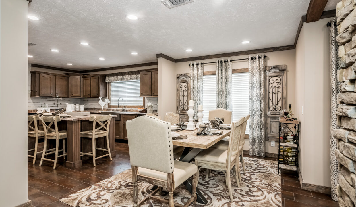 Warm and cozy dining room with a wooden table set for six. Rustic kitchen in the background, stone accent wall, patterned rug, and elegant curtains.