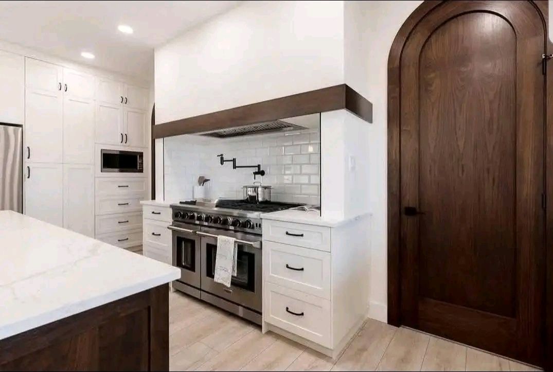 Modern kitchen with a large stainless steel oven, white cabinets, and a dark wooden arched door. Bright, clean, and elegant design.
