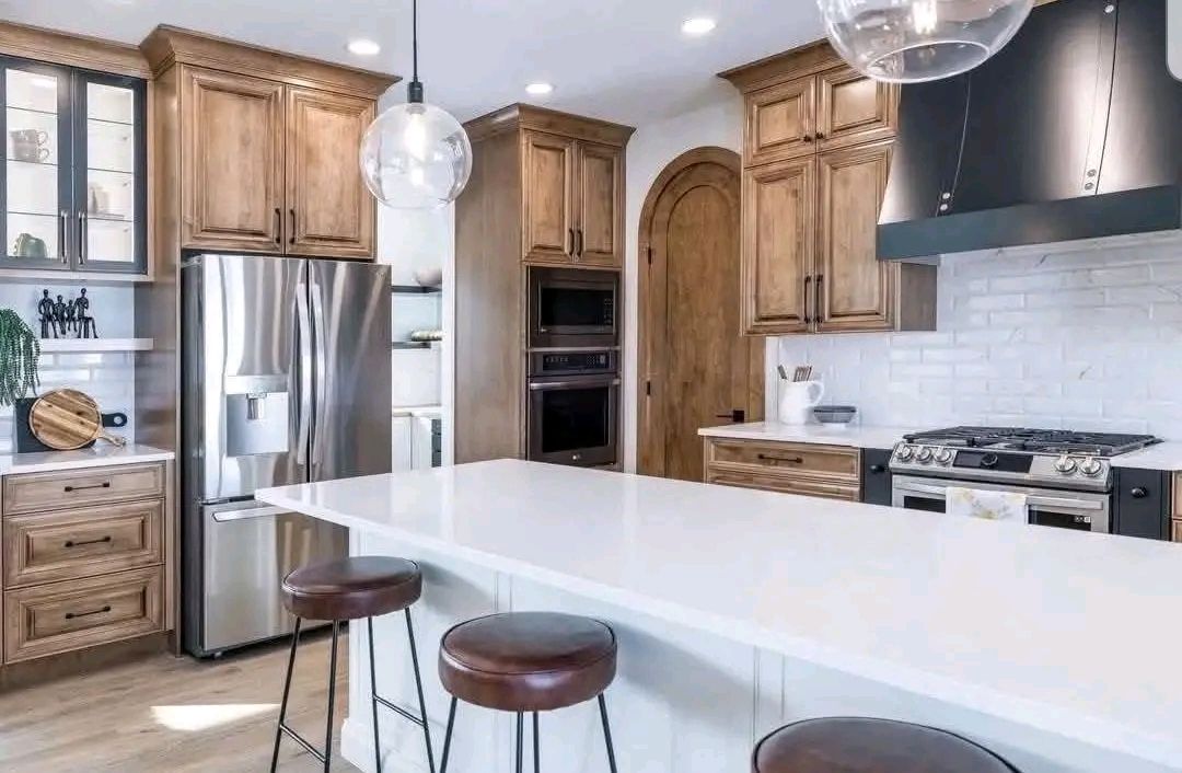 Modern kitchen with wooden cabinets, stainless steel fridge, and a white countertop island with three brown bar stools. Bright, clean, and inviting.