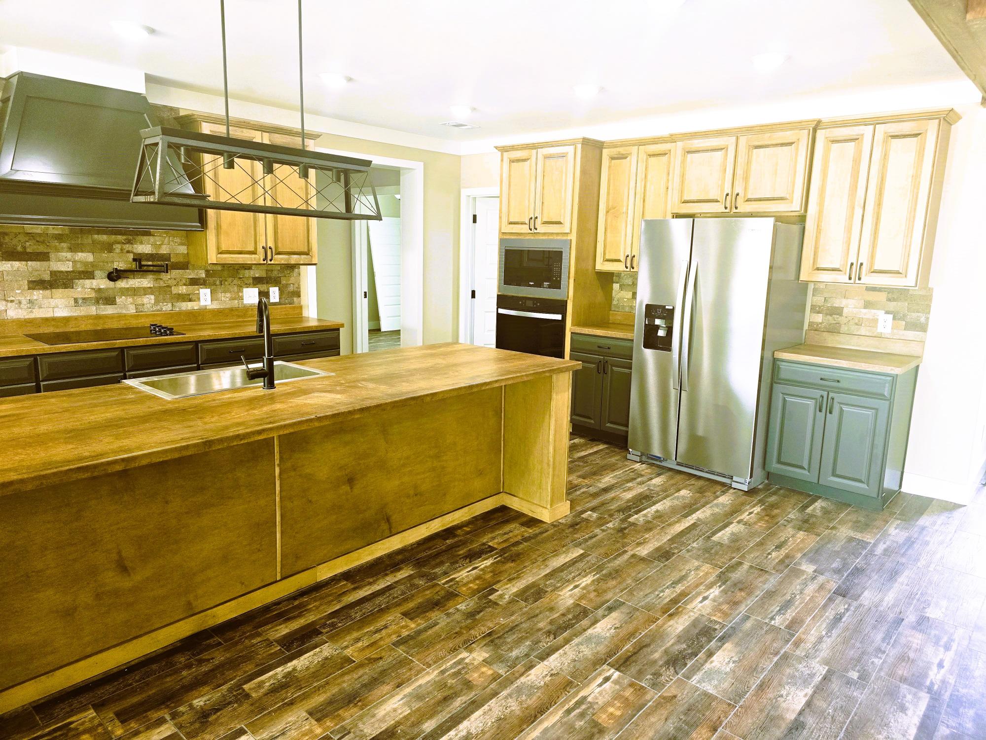 Spacious kitchen with wood cabinets, large island, industrial pendant light, and stainless steel appliances. Warm, rustic, and inviting ambiance.