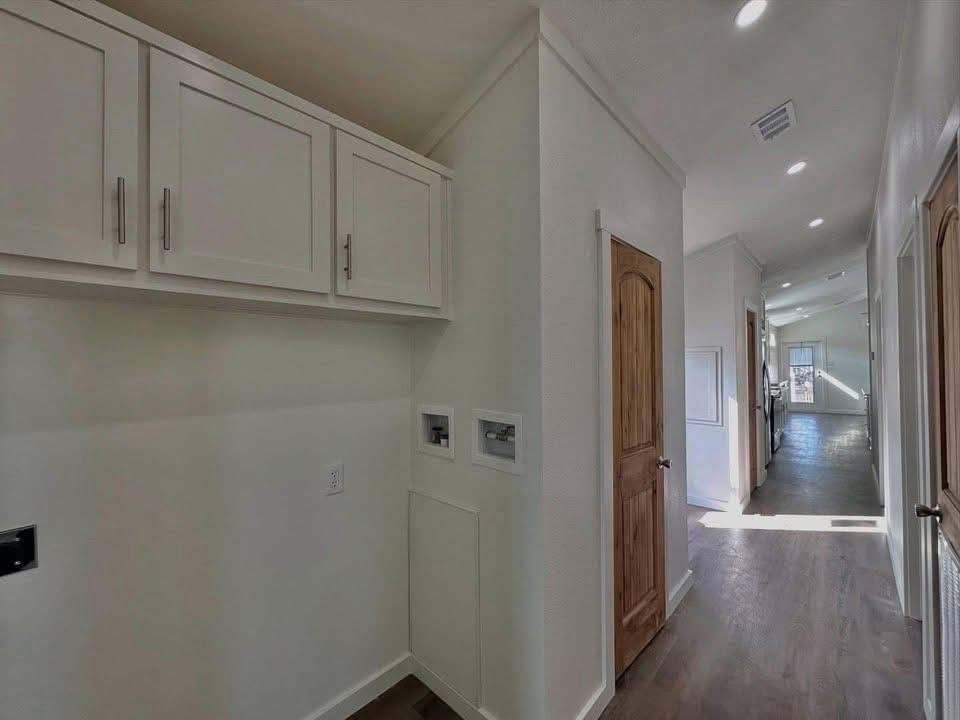 A narrow, sunlit hallway with wooden doors and white walls features overhead storage cabinets. Natural light casts soft shadows on the wood floor, creating a calm ambiance.