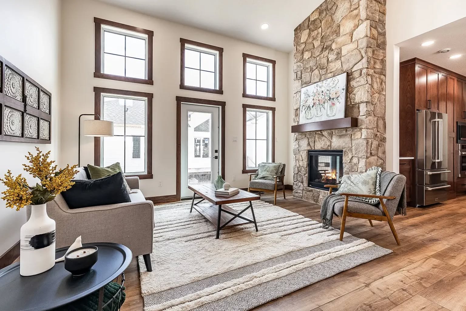 Spacious living room with high ceilings, stone fireplace, and large windows. Cozy seating area with modern furniture, neutral tones, and wooden accents.