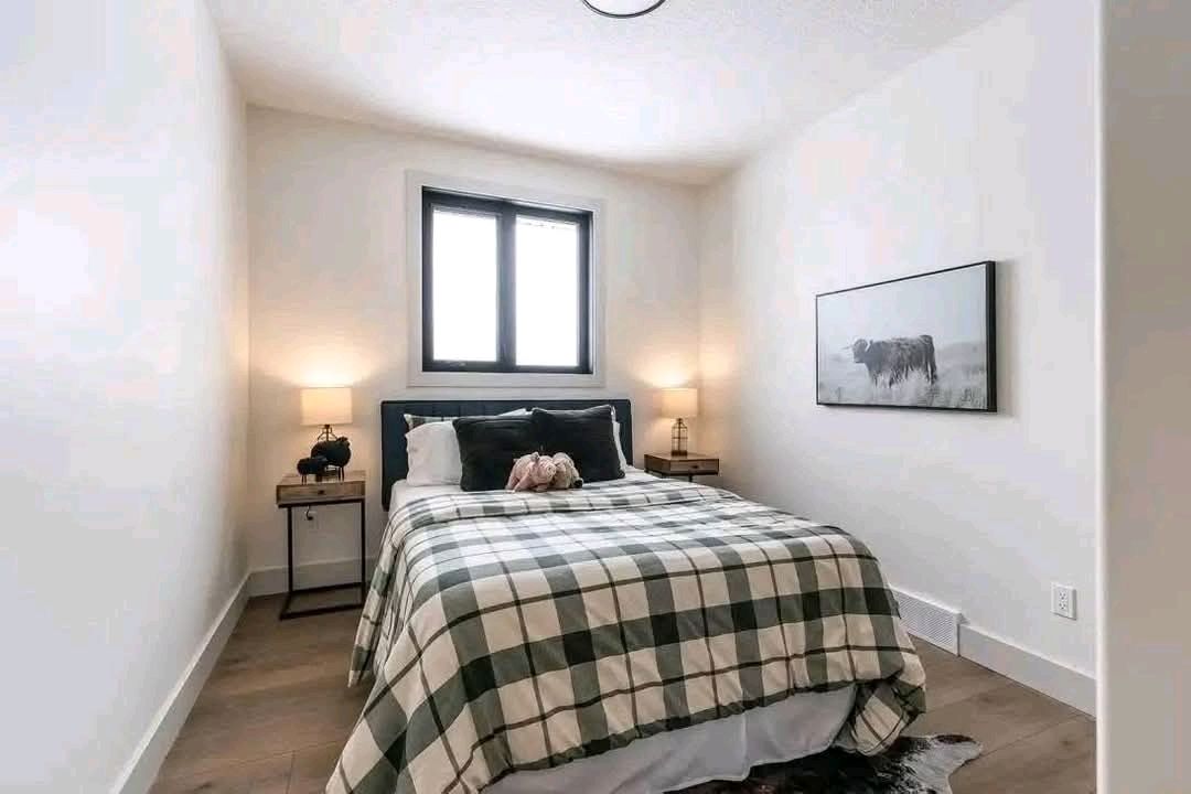 Cozy bedroom with a plaid bedspread, flanked by two lit lamps on wooden nightstands. A framed cow print hangs on a white wall, exuding a serene ambiance.
