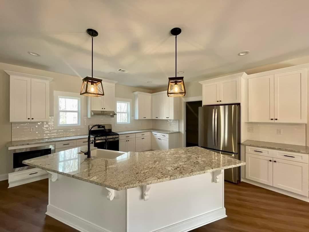 Spacious kitchen with white cabinets, stainless steel appliances, and a large granite island. Warm lighting and wood floors create an inviting feel.