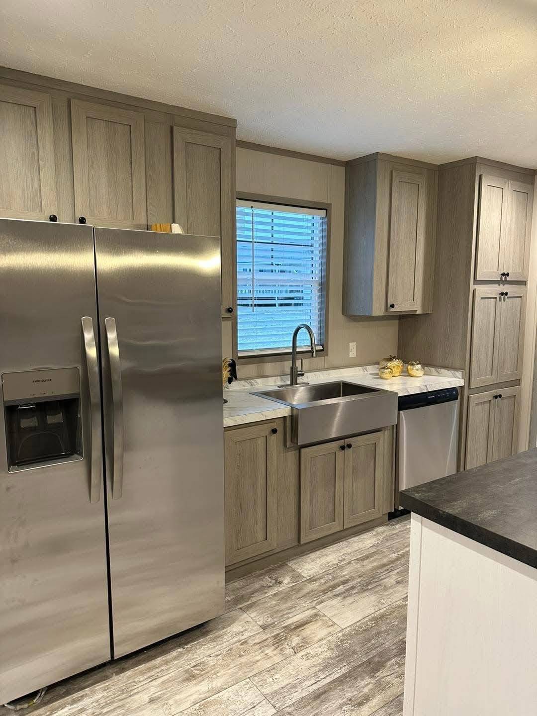 Modern kitchen with gray wood cabinets, a stainless steel fridge, and a farmhouse sink. Light walls, hardwood floors, subtle and cozy ambiance.