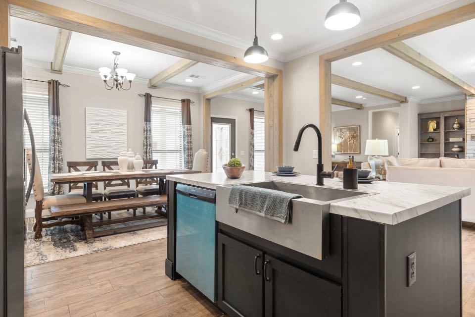 Open-concept kitchen and dining area with wooden beams, modern pendant lights, and hardwood floors. Features a farmhouse sink, central island, and rustic dining table creating a cozy atmosphere.