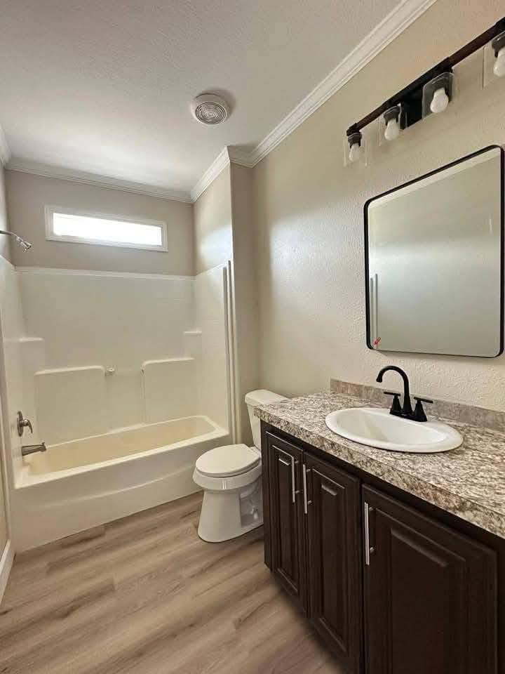 Bright bathroom with beige walls and wood flooring. Features a white bathtub, sink with granite countertop, dark vanity, and wall mirror under lighting.