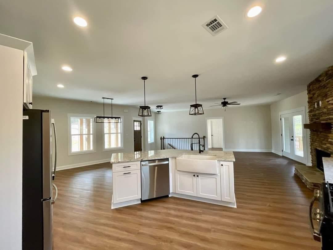 Spacious open-concept living area with a modern kitchen featuring a center island. Wooden floors, cozy stone fireplace, and soft natural light create a warm ambiance.