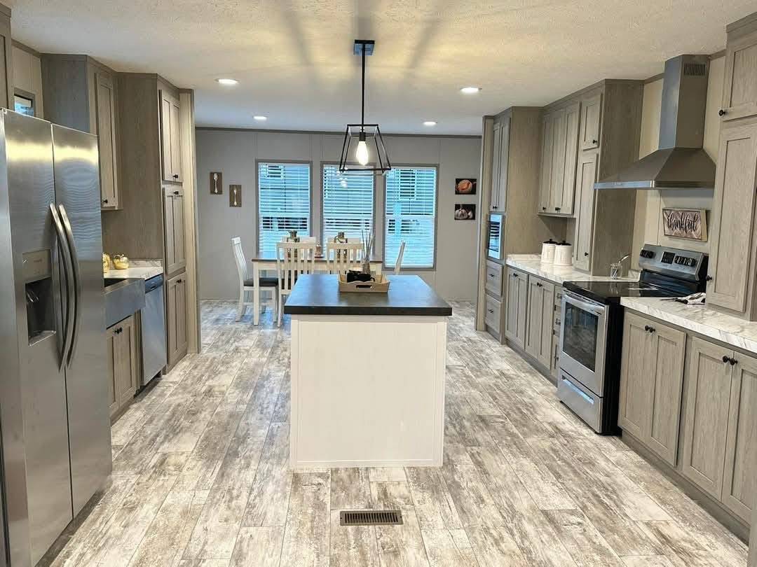 A modern kitchen with rustic charm featuring light wood cabinetry, a central island, stainless steel appliances, and a dining table under soft lighting.