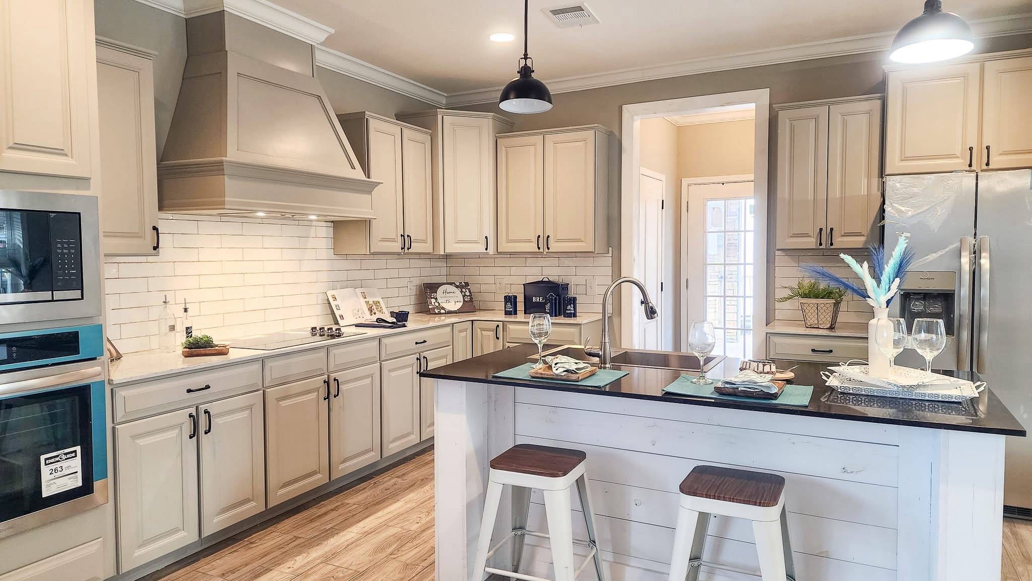 A modern kitchen with beige cabinets, stainless steel appliances, a central island with bar stools, and a warm, inviting atmosphere.