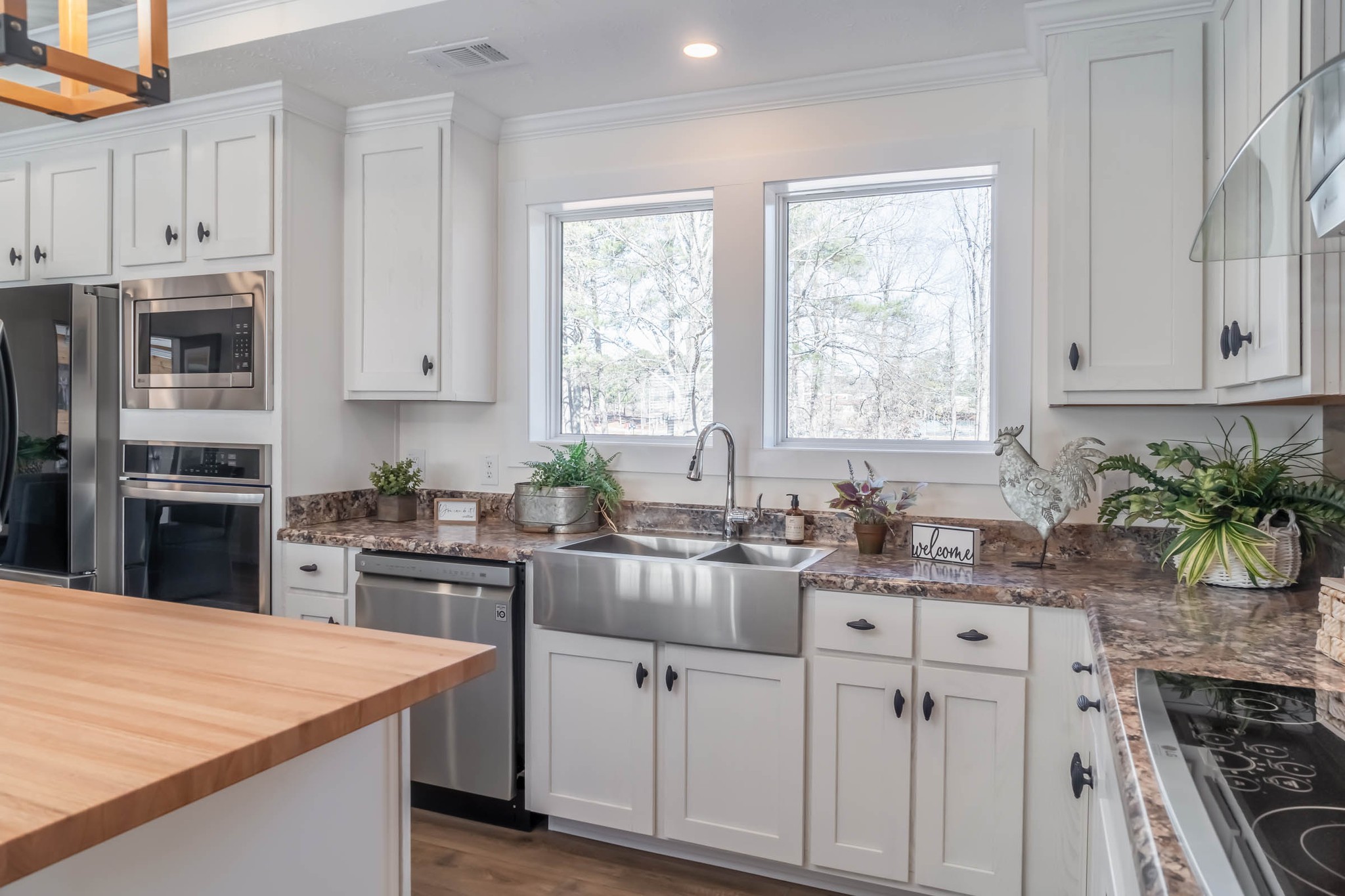 Modern kitchen with white cabinets, stainless steel appliances, and farmhouse sink. Wooden island counter adds warmth. Bright natural light from windows.