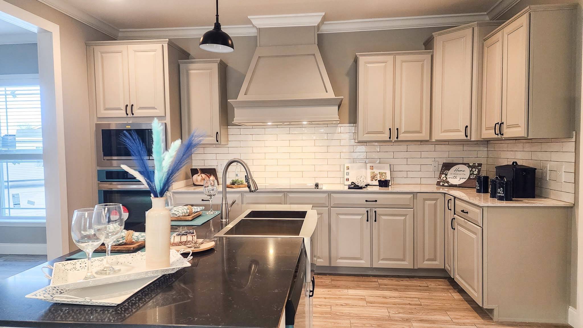 Modern kitchen with white cabinets, subway tile backsplash, and a black countertop. A vase with blue feathers and wine glasses sit on the island. Bright and inviting ambiance.