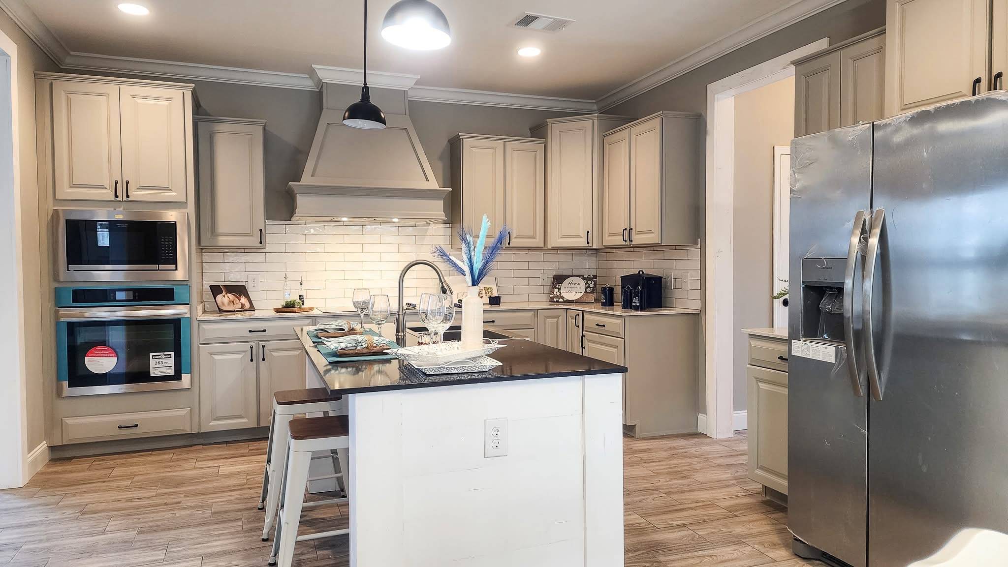 Modern kitchen with beige cabinets, stainless steel appliances, a central island with bar stools, and light wood flooring. Bright, cozy atmosphere.