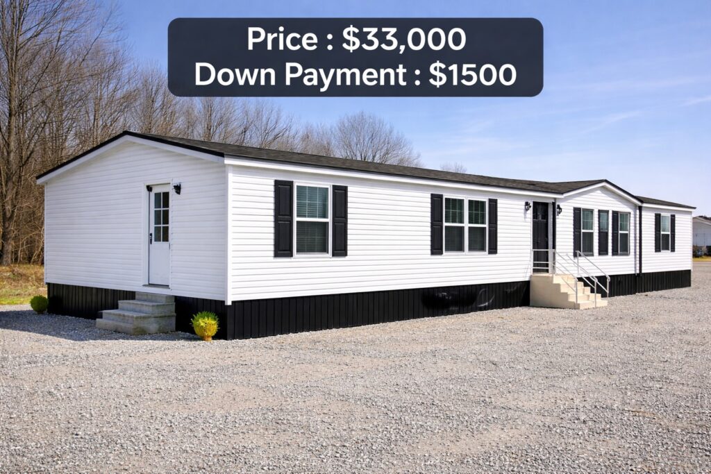 A white manufactured house with black shutters on a gravel lot. Text overlay reads "Price: $33,000, Down Payment: $1,500." Trees are in the background.