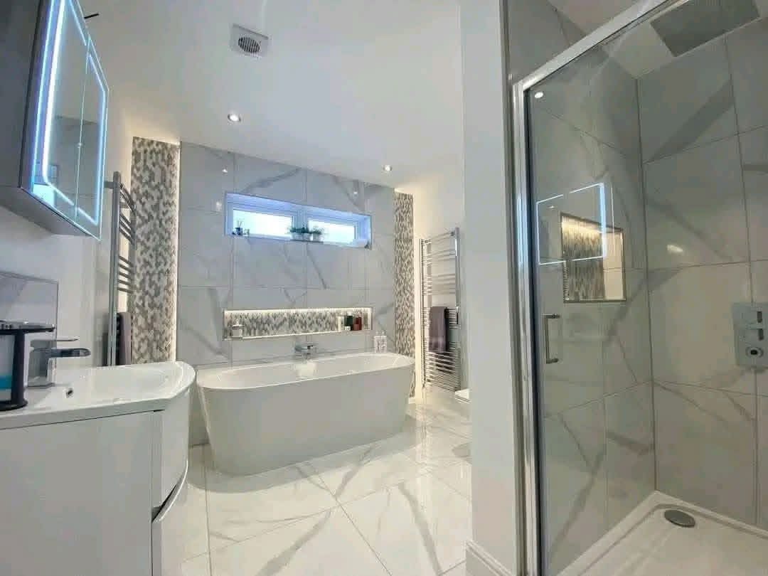 Modern bathroom with a sleek freestanding tub, glass-enclosed shower, and white marble tiles. Soft lighting creates a calm, luxurious atmosphere.