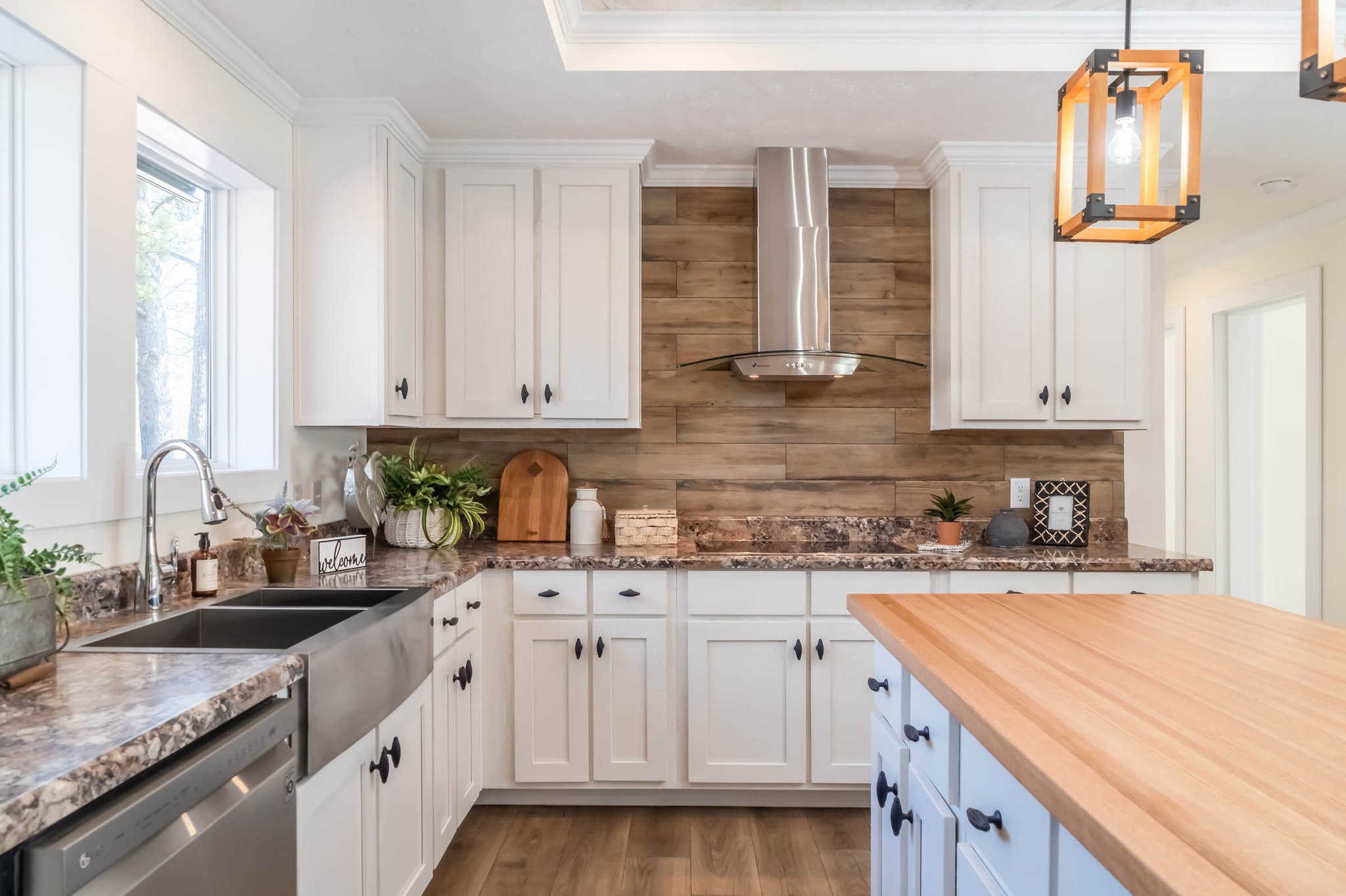 Modern kitchen with white cabinets, stainless steel appliances, wooden backsplash, and a central island with wooden countertop. Warm, inviting ambiance.