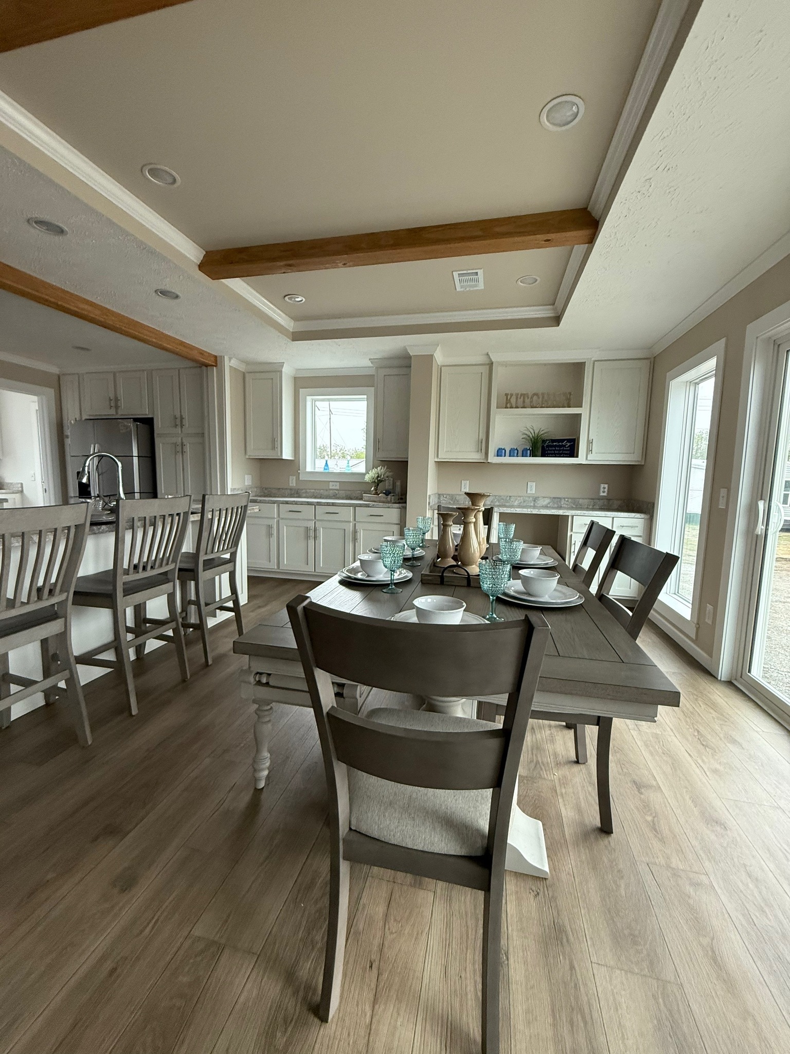 Spacious kitchen with wooden floors, gray cabinets, and a long dining table set for eight with turquoise glasses and white dishes, creating an inviting ambiance.