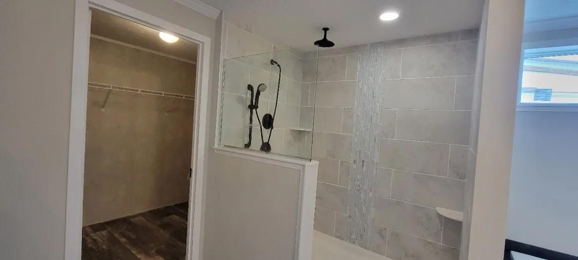 Modern bathroom with a glass-enclosed shower featuring a rain showerhead and hand-held nozzle. Adjacent is an open, walk-in closet. Neutral tones create a clean, serene feel.