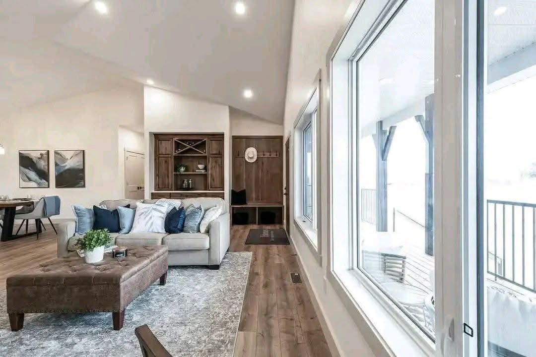 Spacious living room with a cozy beige sofa, blue pillows, and a wooden coffee table. Large windows overlook a bright patio, creating an inviting ambiance.