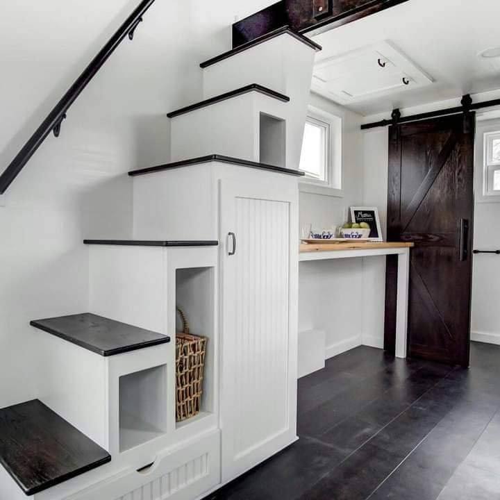 White staircase with black steps in a modern interior, featuring built-in storage cubbies. Nearby, a wooden sliding barn door and small desk create a cozy, efficient space.