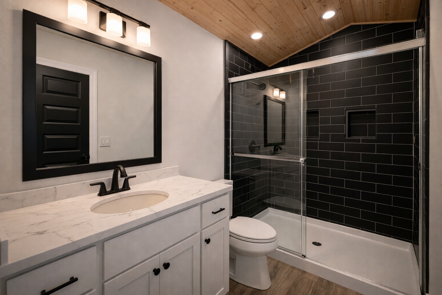 Modern bathroom with a sleek design. Features a white vanity with a marble countertop, black fixtures, large black tile shower, and warm wood ceiling.