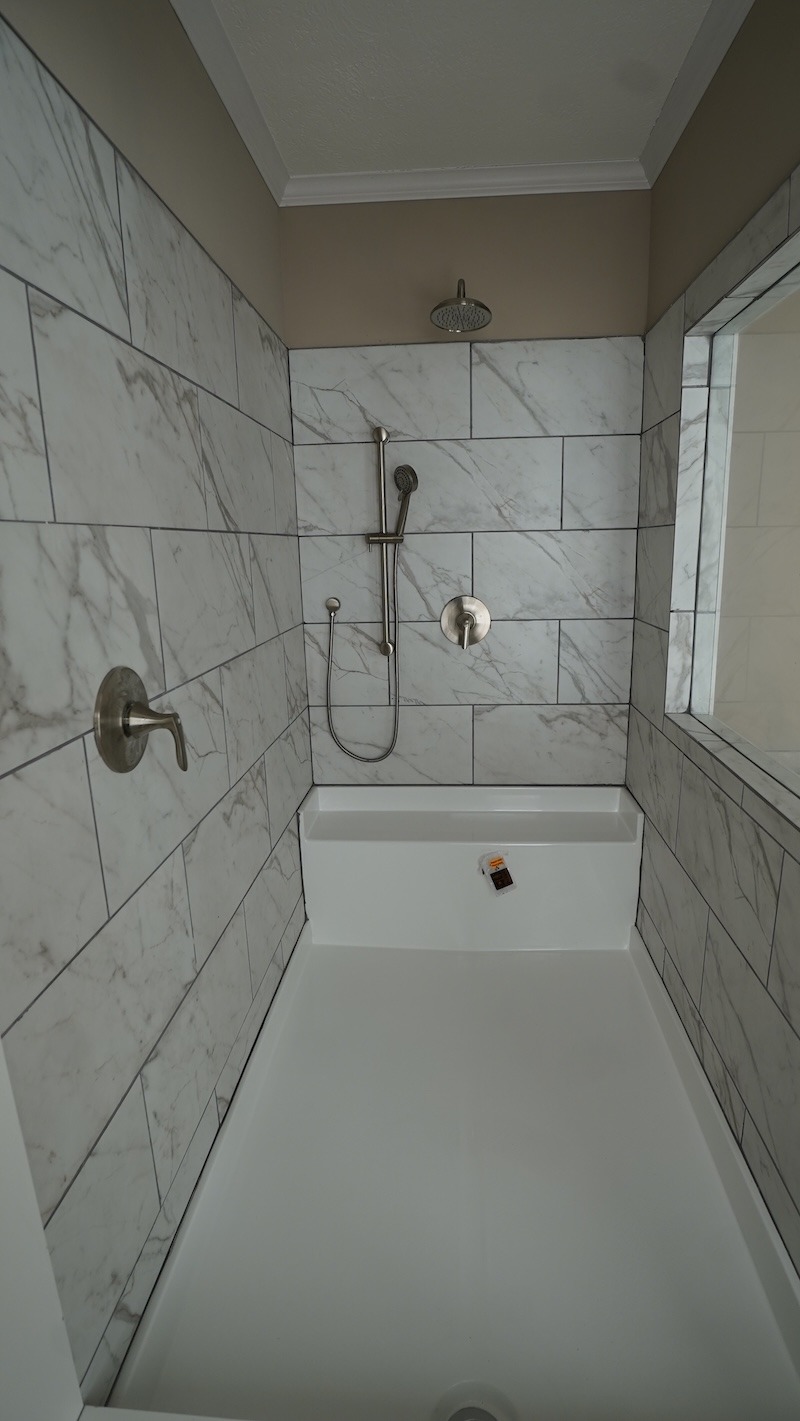 Modern bathroom with white marble-tiled shower walls, chrome fixtures, and a sleek rain showerhead, creating a clean and minimalist ambiance.