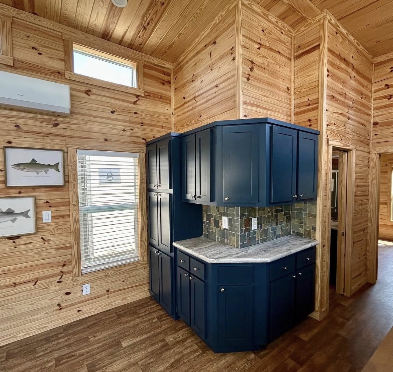 High-end housing showcase featuring a diverse collection of modern manufactured homes, tiny homes, and park models, including the expansive "The Boujee XL" aesthetic.

Exterior Architectural Styles: Highlights include a classic white board-and-batten tiny home with a grand pillared front porch and black metal railings, alongside a sage green model with similar farmhouse features. A standout premium model features a striking dark charcoal exterior with a copper-tone metal roof, natural cedar wood accents, and a large wrap-around elevated wooden deck. Also featured are traditional manufactured homes with tan vinyl siding, decorative red shutters, and spacious covered front porches.

Interior Living & Custom Design: Open-concept interiors are defined by high-fidelity finishes, including vaulted ceilings with rustic dark wood beams or light natural wood planks. Living spaces showcase a "modern boujee" style with neutral-toned sofas, integrated electric fireplaces, and lofted sleeping quarters with black metal balustrades. Rustic cabin-style interiors feature all-over natural wood walls and ceilings, complemented by modern navy blue cabinetry.

Gourmet Kitchens & Dining: The collection features diverse kitchen layouts, including minimalist tiny home kitchens with natural wood cabinetry and high-end modern designs. Premium features include oversized kitchen islands, marble-look or dark stone countertops, farmhouse-style cabinetry in deep navy or white, and professional-grade stainless steel appliances. Modern lighting includes elegant pendant chandeliers and black industrial-style ceiling fans.

Spa-Inspired Bathrooms & Bedrooms: Bathrooms emphasize modern luxury with walk-in tile showers featuring marble-look surrounds, black matte or brushed nickel hardware, and contemporary grey vanities with ample storage. Bedrooms offer clean, minimalist designs with neutral carpeting and large windows for natural light. This gallery represents the pinnacle of "boujee" manufactured living, combining versatile floor plans with sophisticated, modern farmhouse aesthetics.