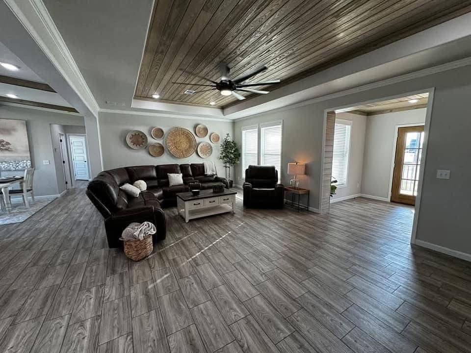 Spacious living room with a dark leather sectional, recliner, and a basket of blankets on wood flooring. A ceiling fan complements the cozy ambiance.
