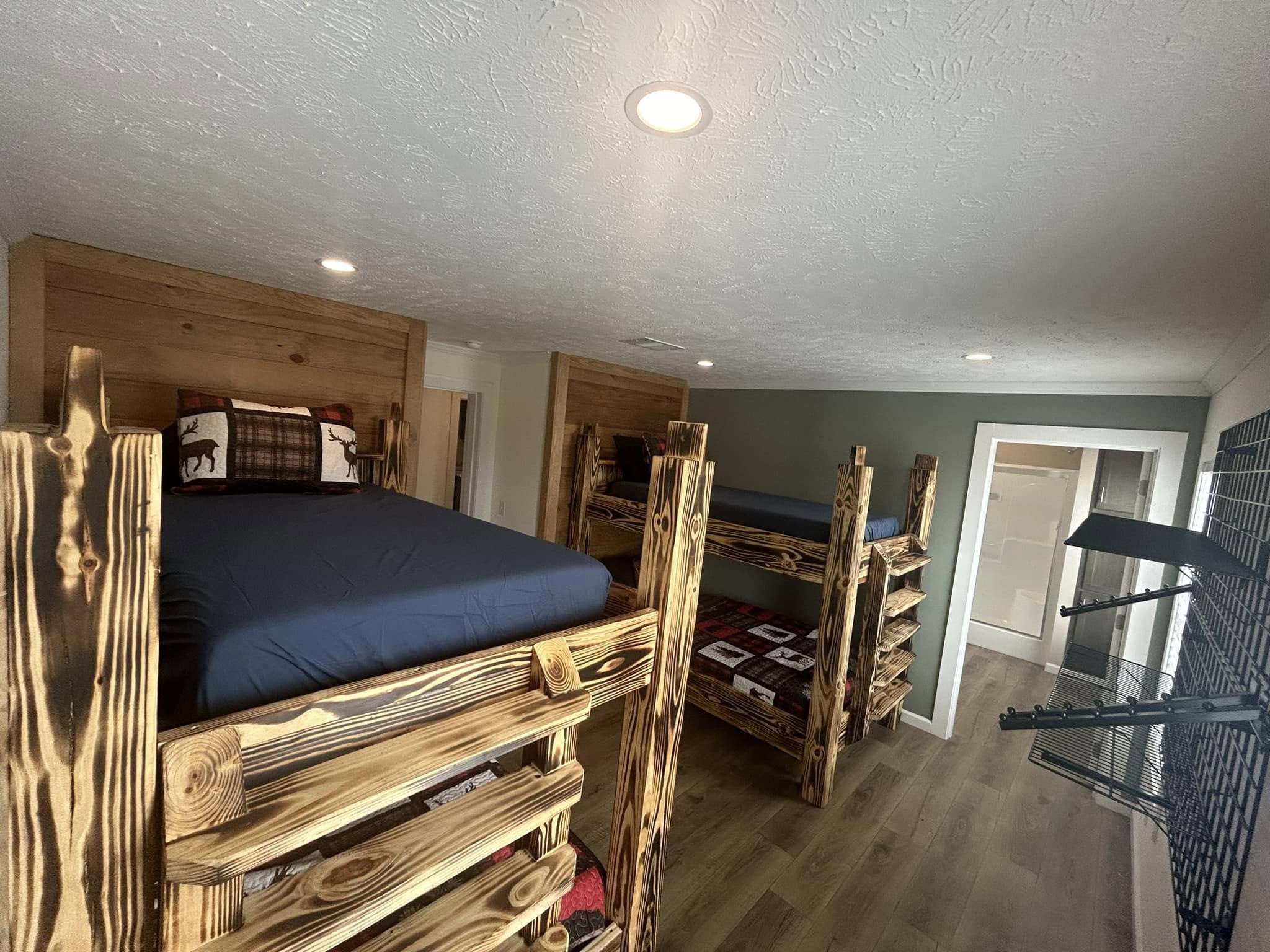 Rustic bedroom with two wooden bunk beds featuring plaid bedding. Wood-paneled walls and a wooden floor create a cozy, cabin-like atmosphere.