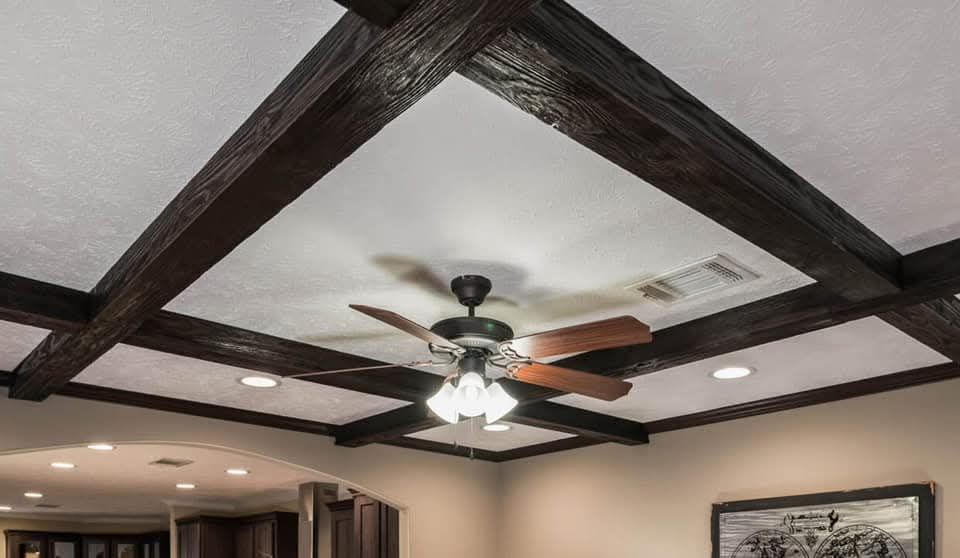 Ceiling with dark wooden beams forming a grid pattern. A ceiling fan with wooden blades and a light fixture is centered. The room has recessed lighting.