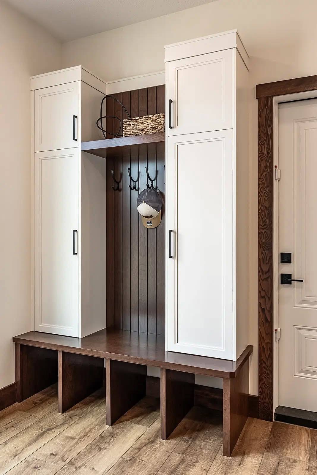 Mudroom area with white cabinets, dark wood bench, and storage cubbies. Hooks hold a cap and basket, creating a neat, welcoming entryway.