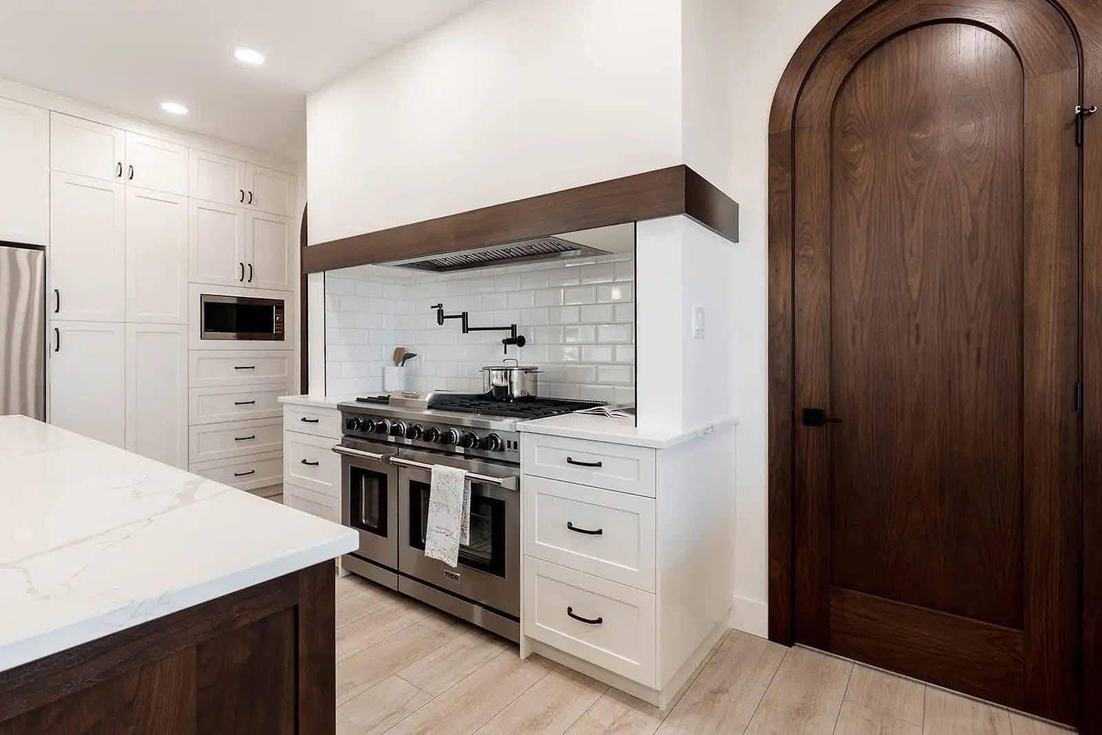 Modern kitchen with a large stainless steel stove and white cabinets. The subway tile backsplash and arched wooden door add a stylish touch.