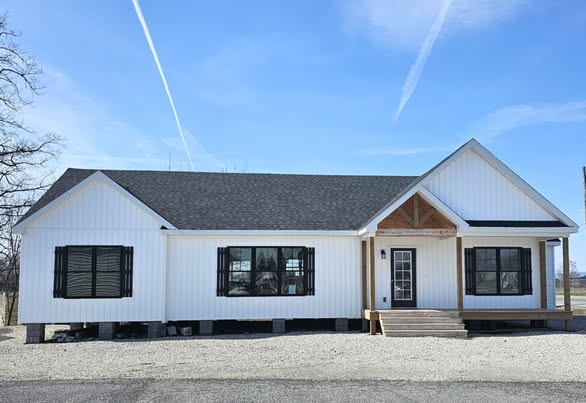 A modern white ranch-style house with black shutters and a gray roof, set under a clear blue sky with contrails. The front door has a small porch with steps leading up. The building conveys a sense of simplicity and tranquility.