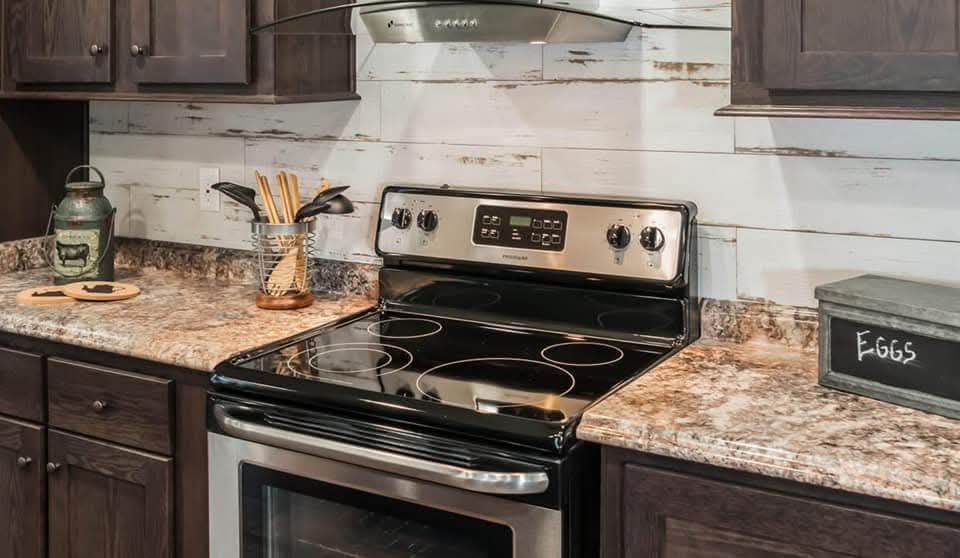 A modern kitchen with a stainless steel electric stove and range hood. Dark wooden cabinets and granite countertops create a warm, rustic ambiance.