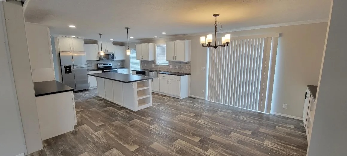 Spacious kitchen and dining area with dark wood flooring. Features white cabinets, stainless steel appliances, a central island, and pendant lights.