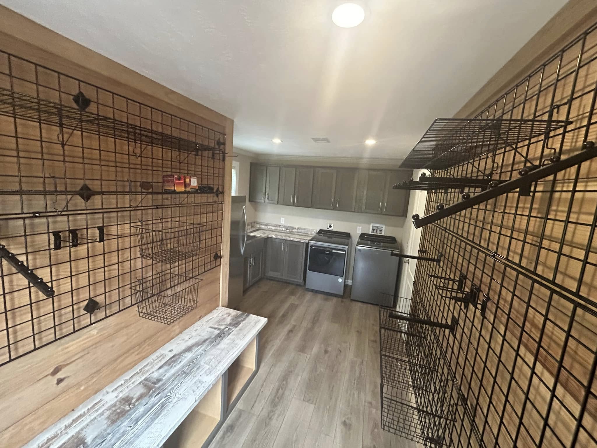 Mudroom with wooden floors, wire racks on walls, bench, and laundry area with washer, dryer, and cabinets. Bright, organized space.