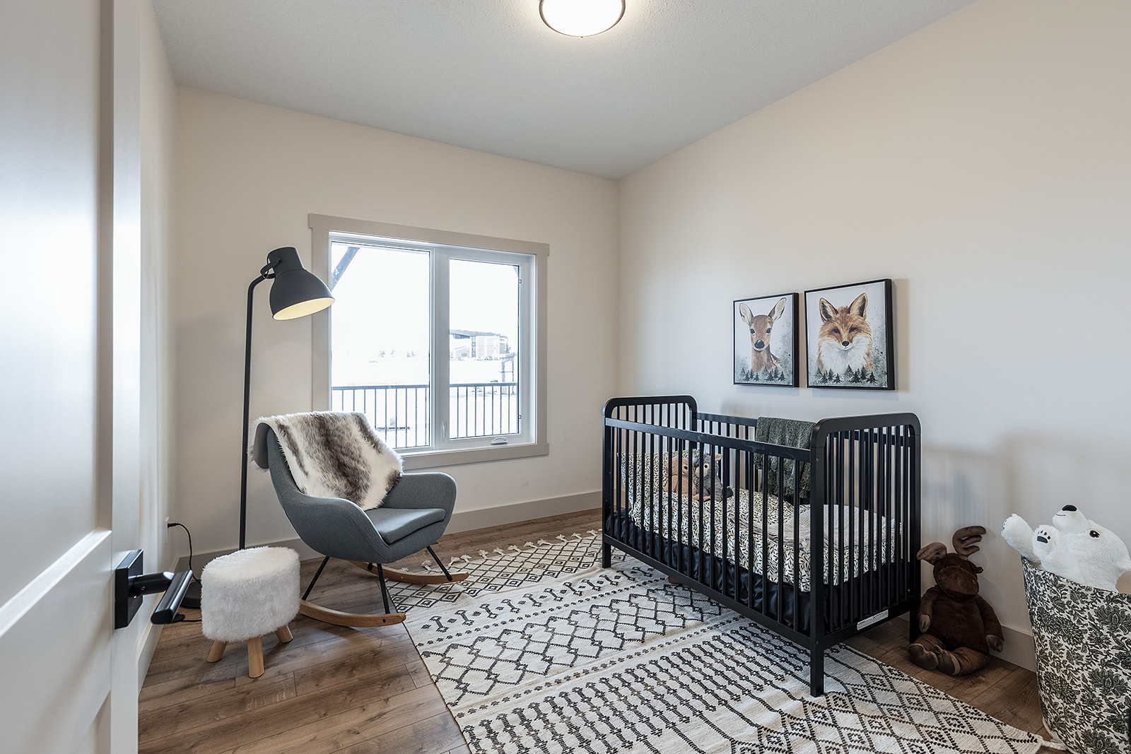 A cozy nursery with a black crib, animal art on the wall, a gray rocking chair, and plush toys. Light pours in through a window, creating a warm ambiance.