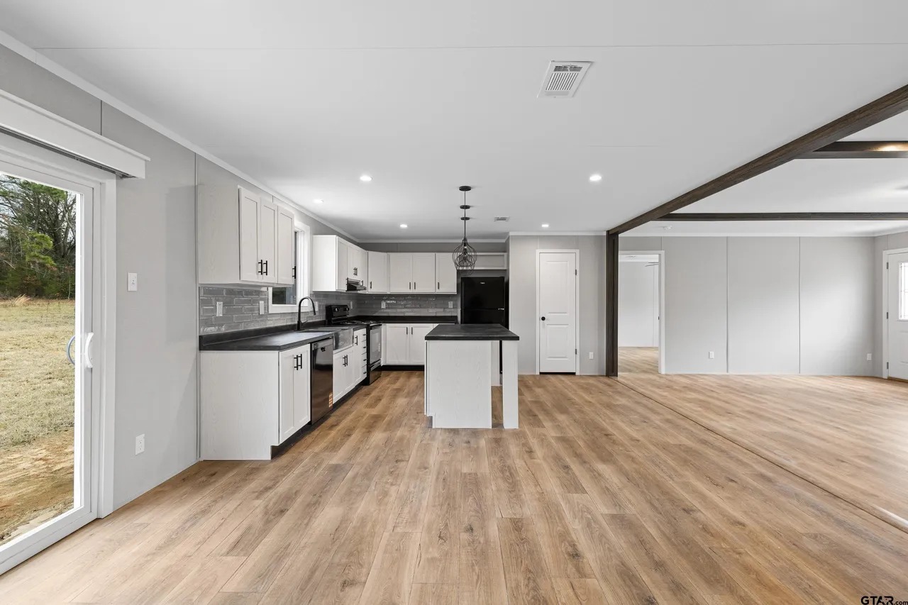 Spacious modern kitchen with white cabinets, dark countertops, and an island. Light wood floors and large windows create an open, airy feel.