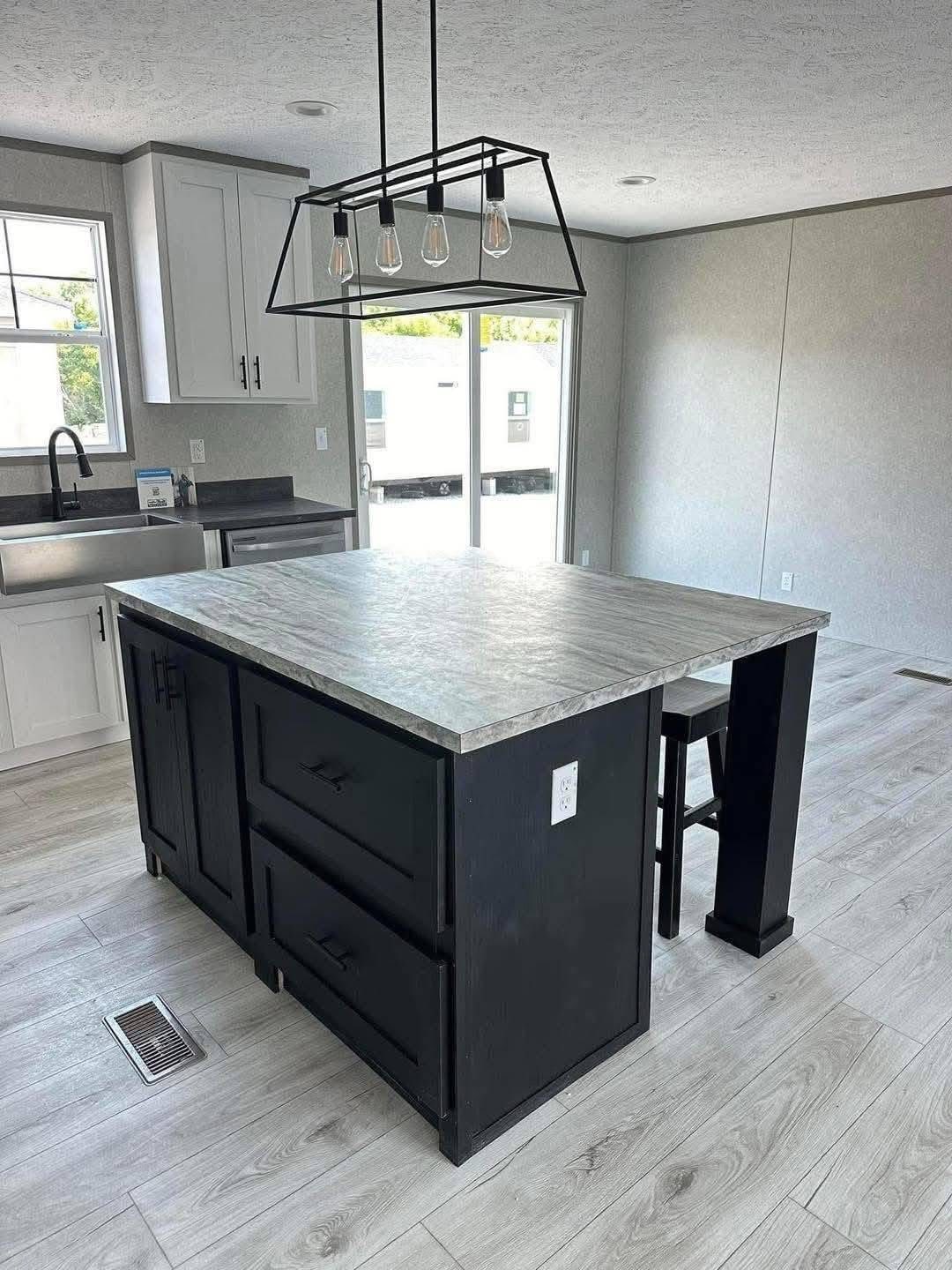 Modern kitchen with a large, dark island featuring a light granite countertop. Overhead, a stylish black pendant light with four bulbs hangs.