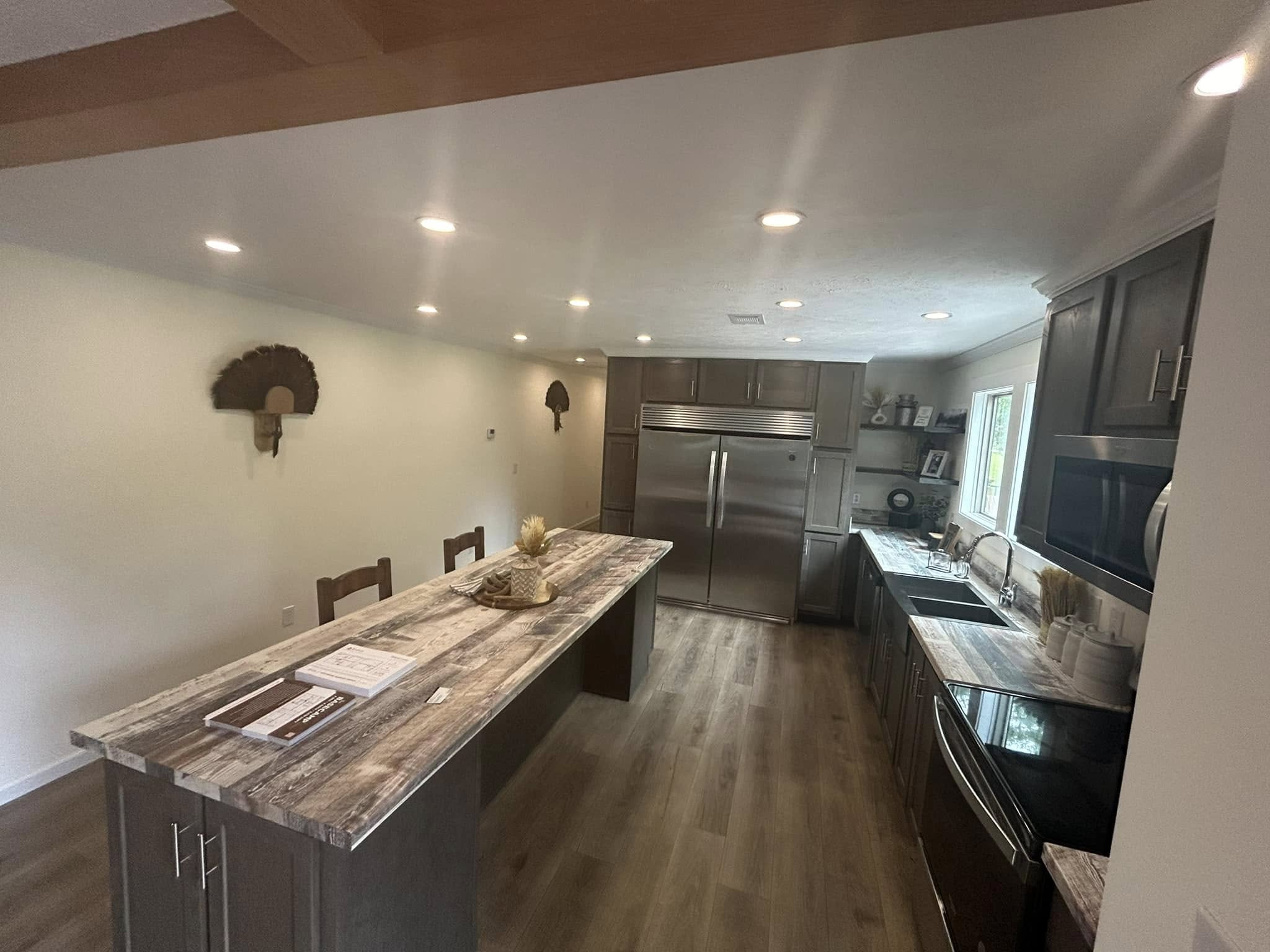 Modern kitchen with wood flooring, a large marble island, and stainless steel appliances. Soft lighting creates a warm, inviting atmosphere.