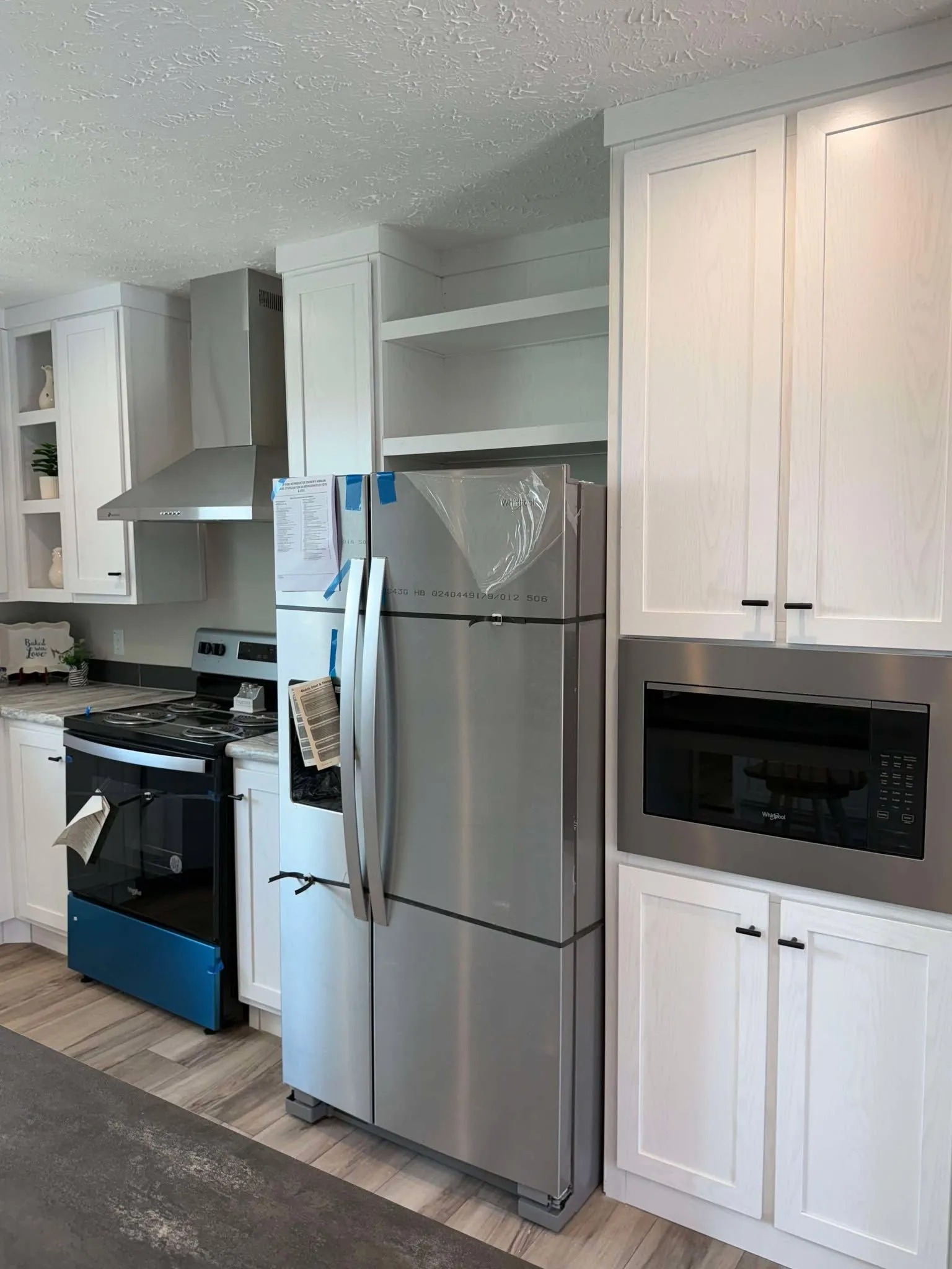 Modern kitchen with a stainless steel fridge, adjacent white cabinets, microwave, and electric stove. Bright, clean, and organized atmosphere.