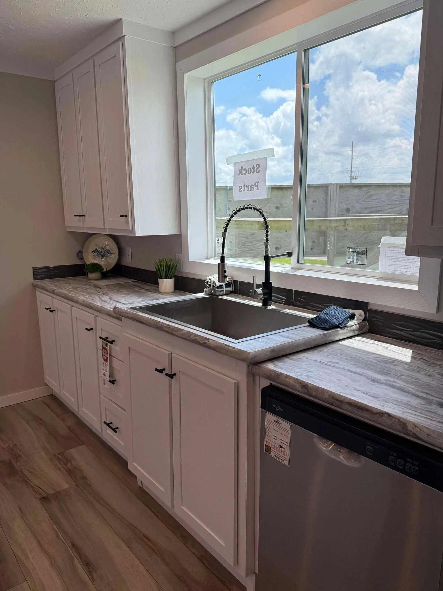 Contemporary kitchen with white cabinets, marble countertop, and stainless steel sink. Sunlight streams through a large window, creating a bright, airy feel.