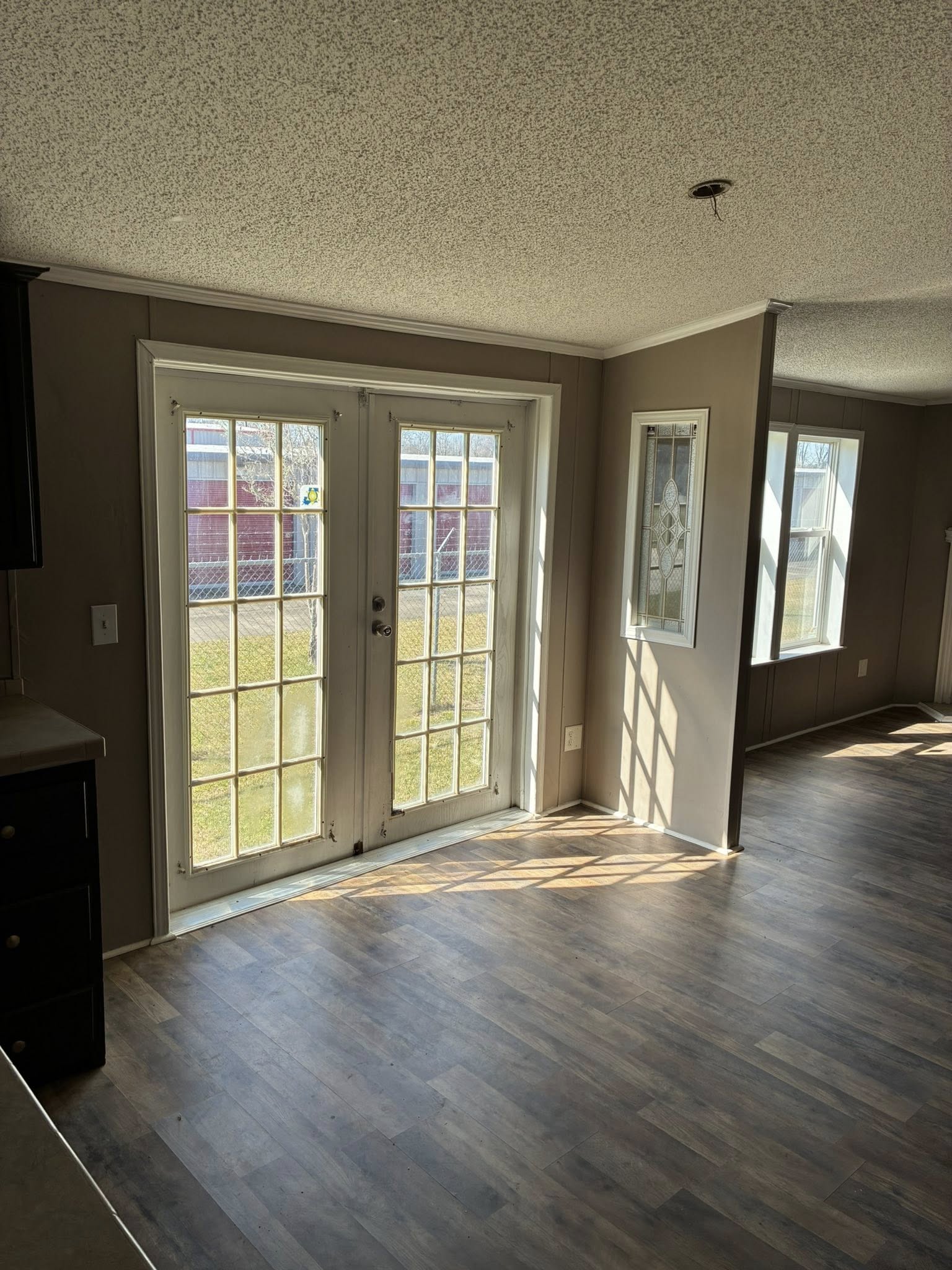 Sunlit room with wooden floors, featuring large French doors leading outside. Soft light filters through, creating a warm and inviting atmosphere.